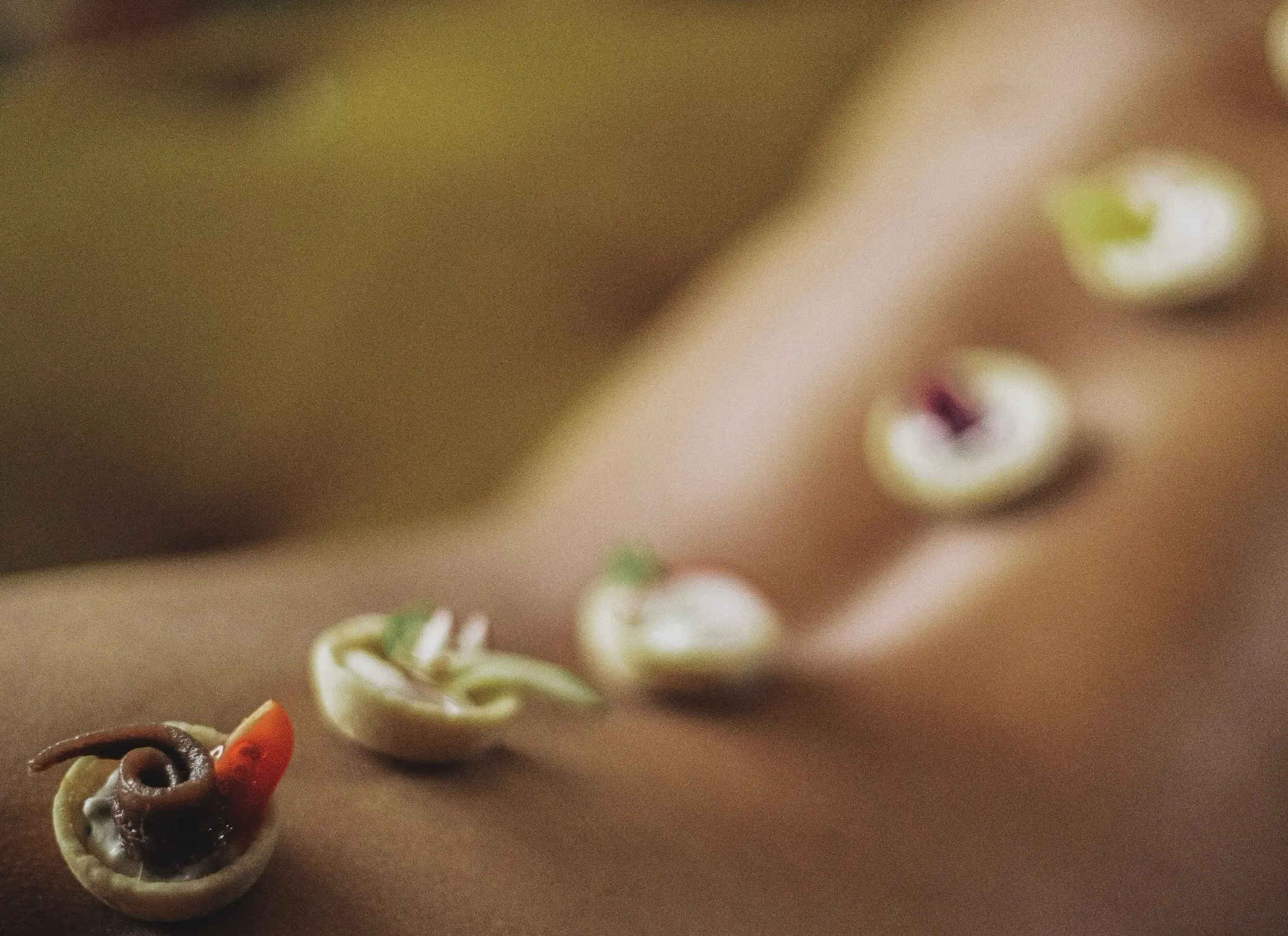 Food art by Lalla Mina: anchovy and tomato tartlets set in a line along a bare back