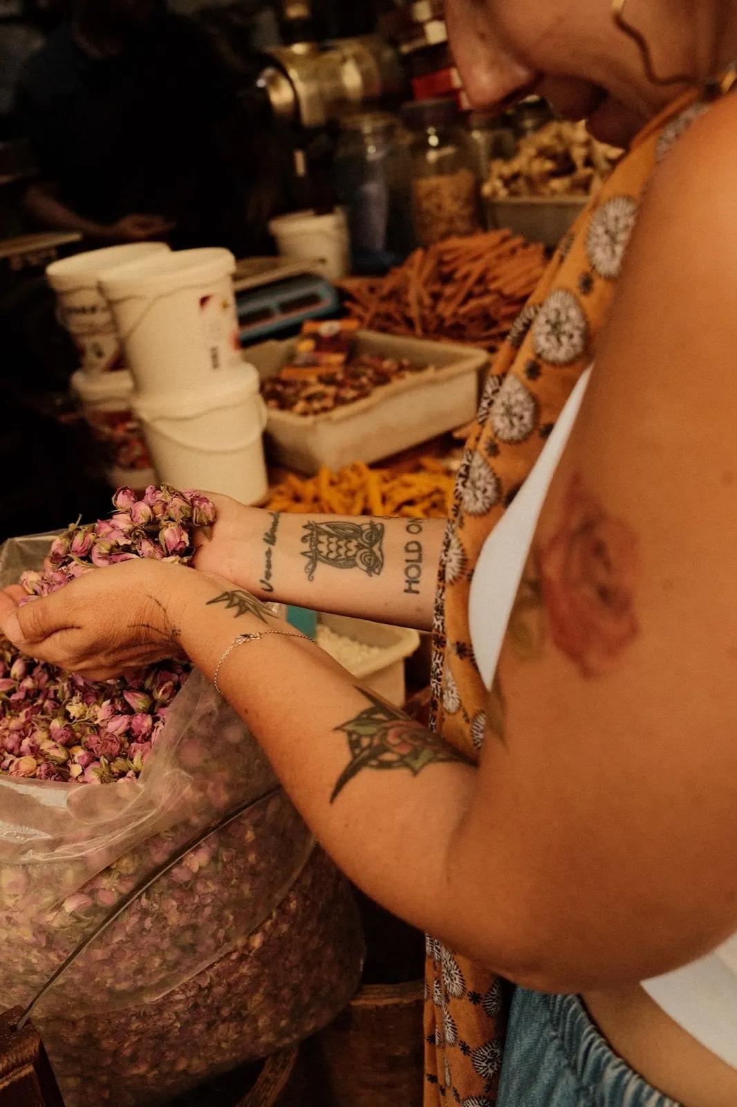 Tattooed hands scooping dried rosebuds at a spice market
