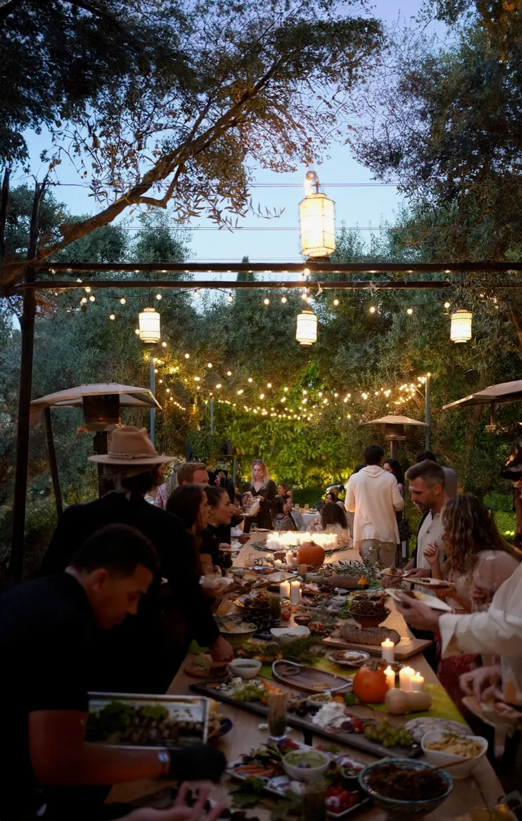 Guests at a lantern-lit feast under olive trees