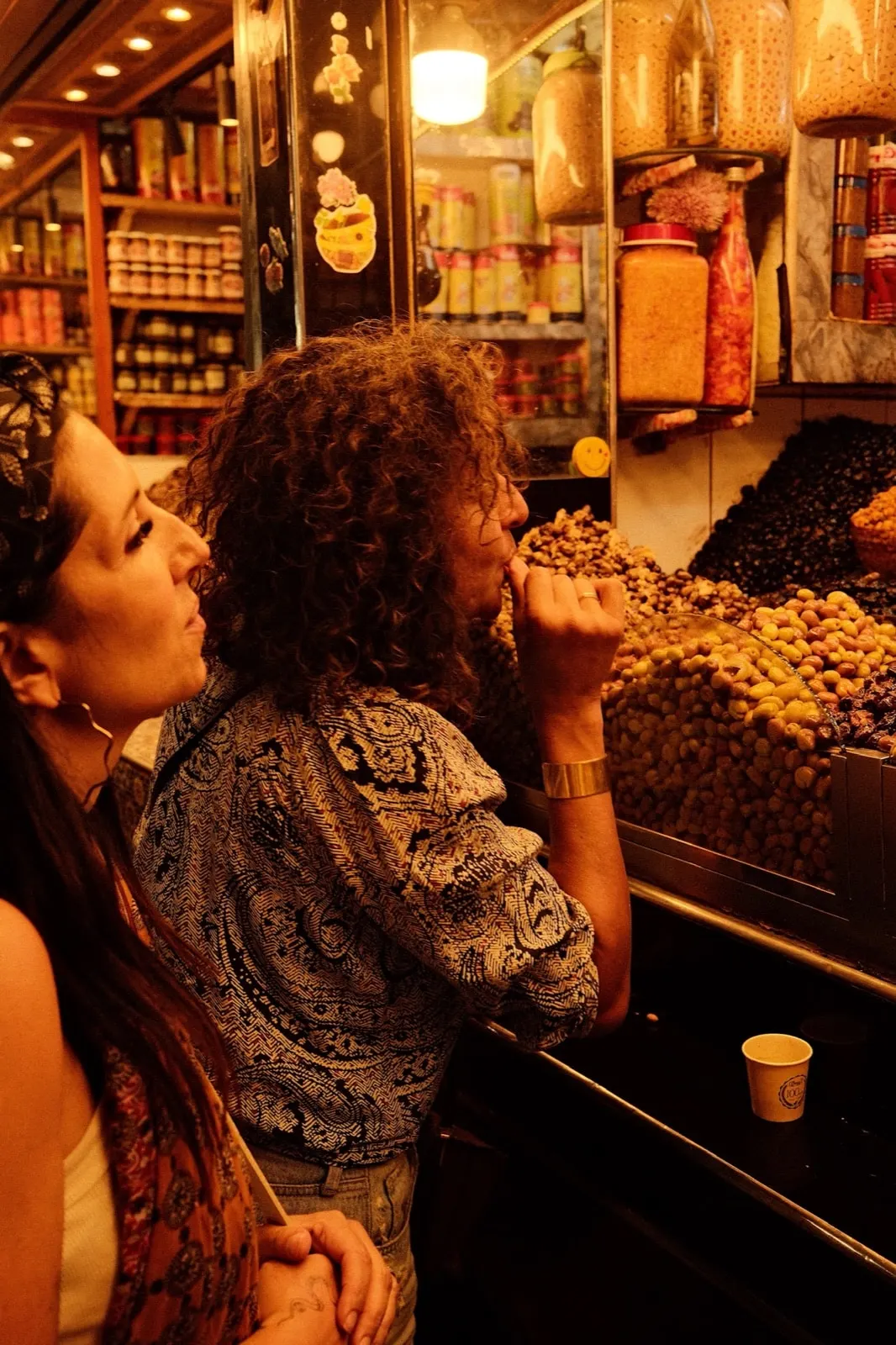 Two women tasting olives at a market stall