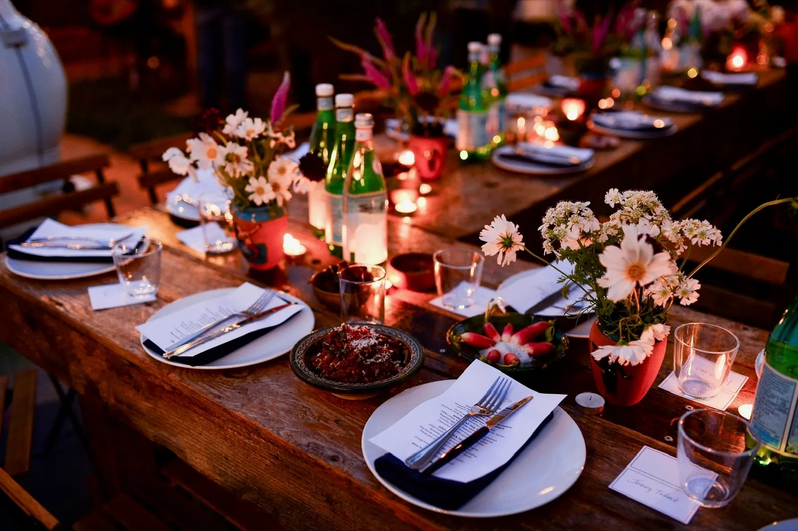 Private dinner table set with menus, candles and daisies in terracotta pots