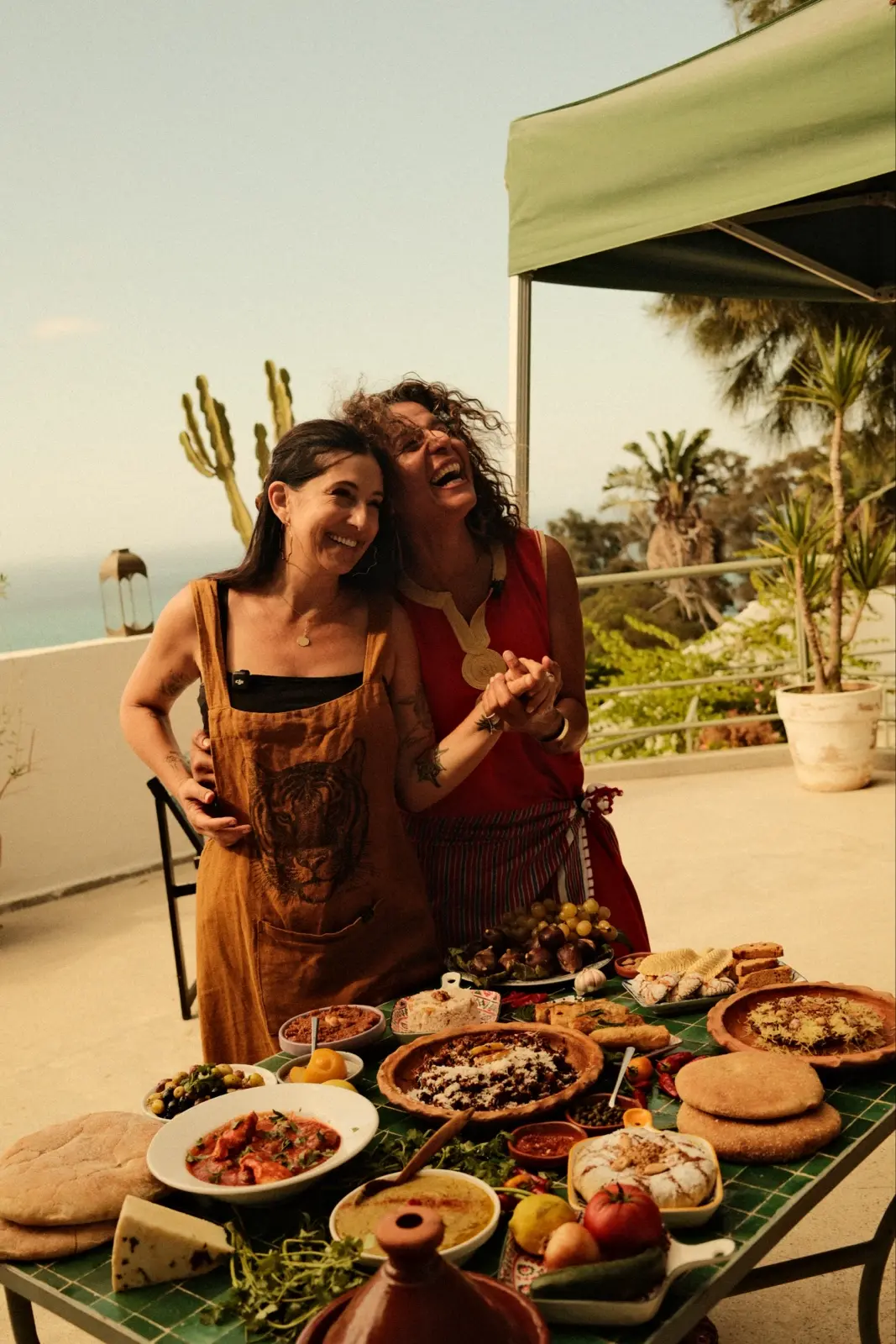 Rose Previte and Yasmina Ksikes laughing behind a feast on a terrace in Tangier