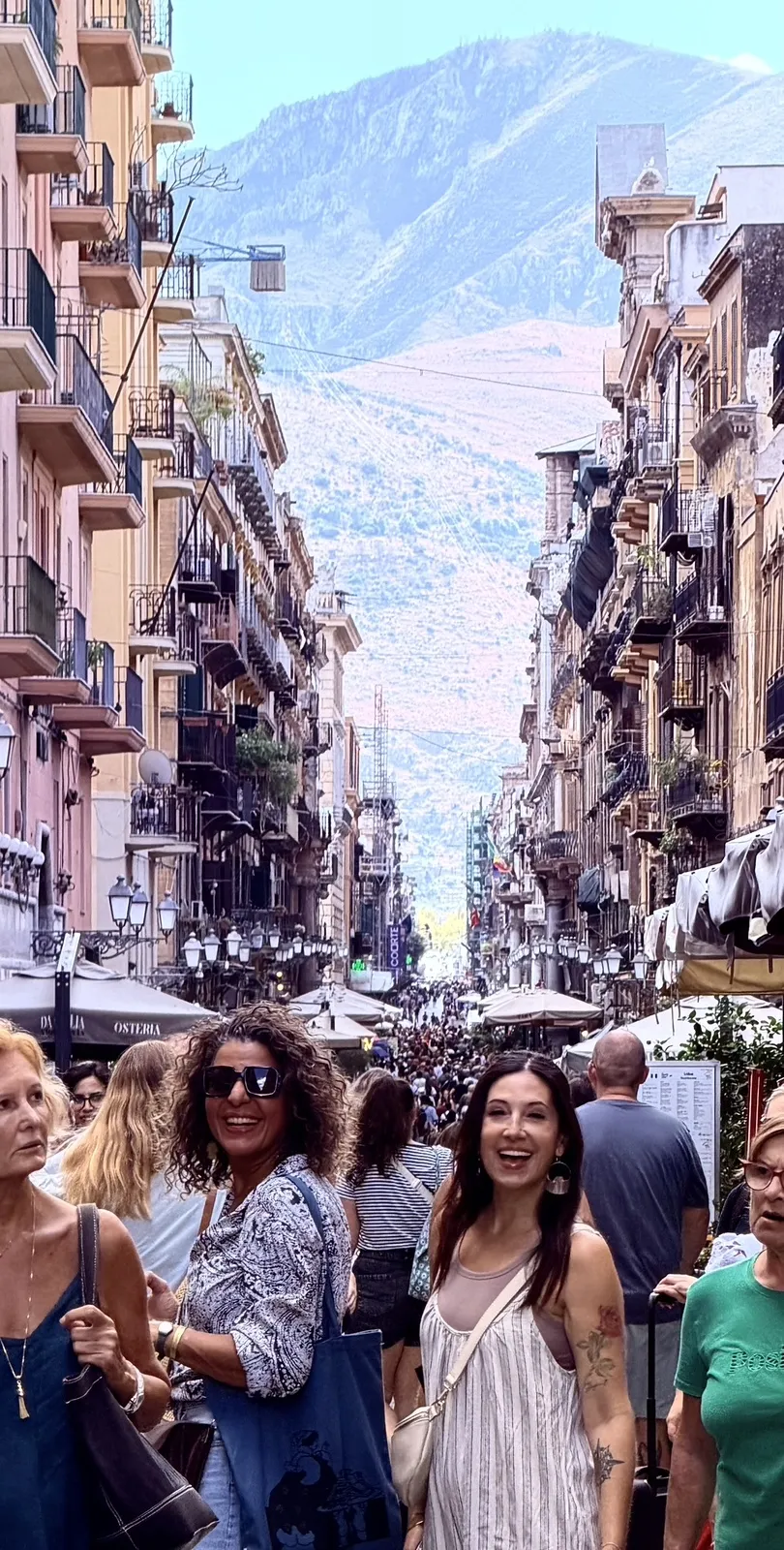 Rose Previte and Yasmina Ksikes smiling in a crowded street in Palermo, mountains behind